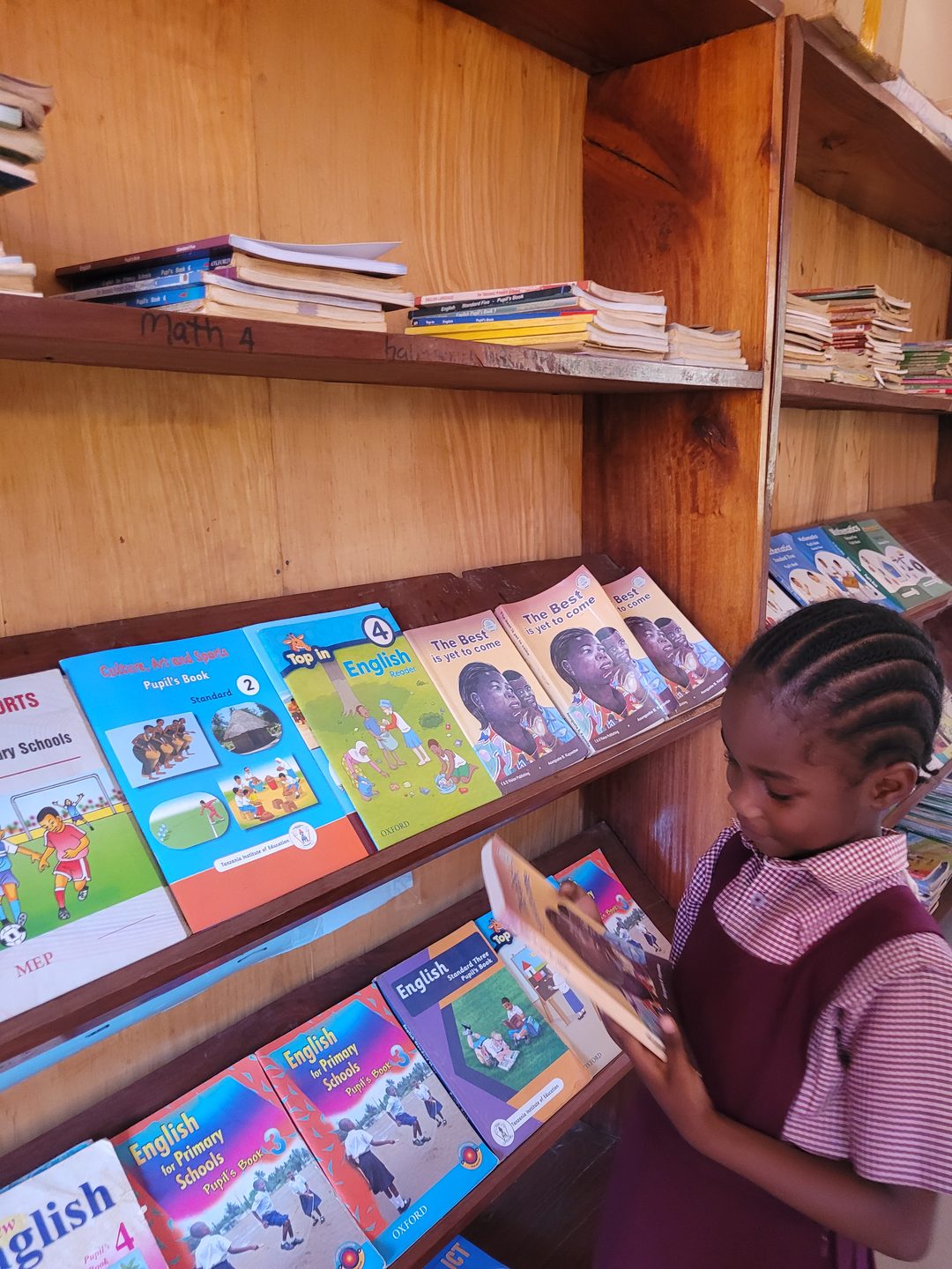 A pupil reading a book beside the school bookshelves
